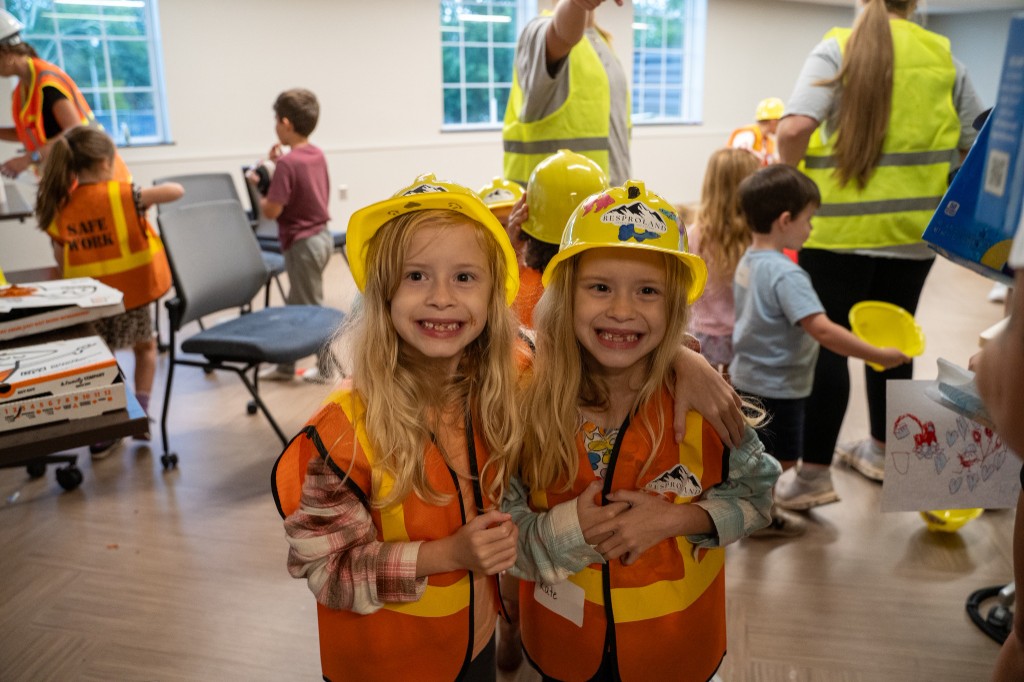 Two girls smiling together in safety vests and hard hats.
